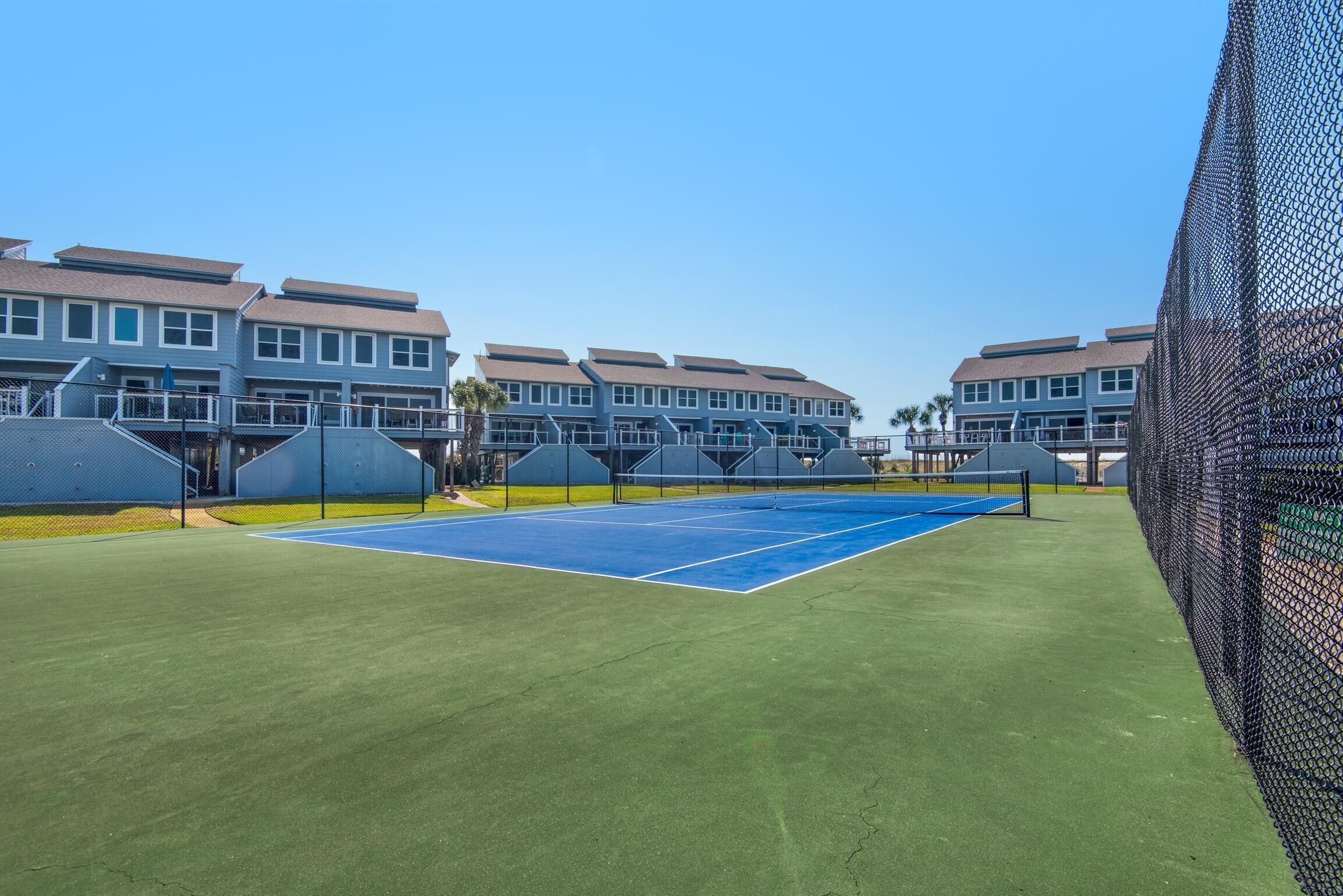 A tennis court with a net, surrounded by buildings with balconies and a clear sky.