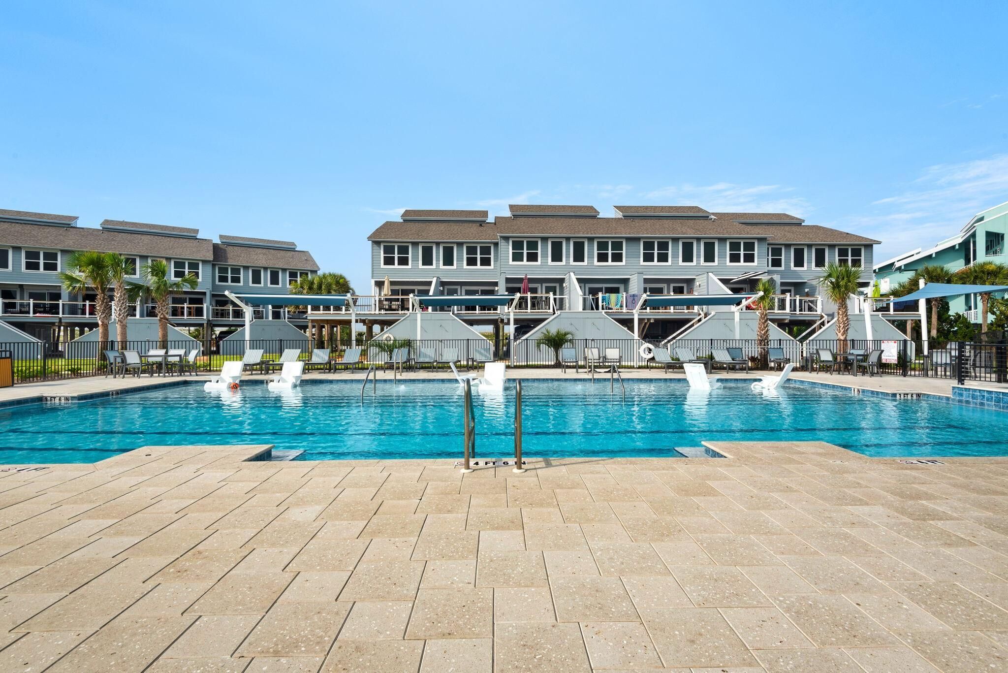 A swimming pool with lounge chairs and a building with multiple balconies in the background.