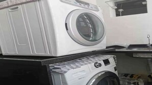 A stacked washer and dryer unit in a kitchen area with a window above the appliances. - Cozy apartment in the best location in Itaim Bibi. (São Paulo)