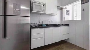 A modern kitchen with white cabinets, a stainless steel refrigerator, a microwave, and a black countertop. - Cozy apartment in the best location in Itaim Bibi. (São Paulo)