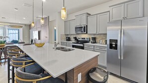 Una cocina moderna con una isla central, electrodomésticos de acero inoxidable e iluminación colgante.