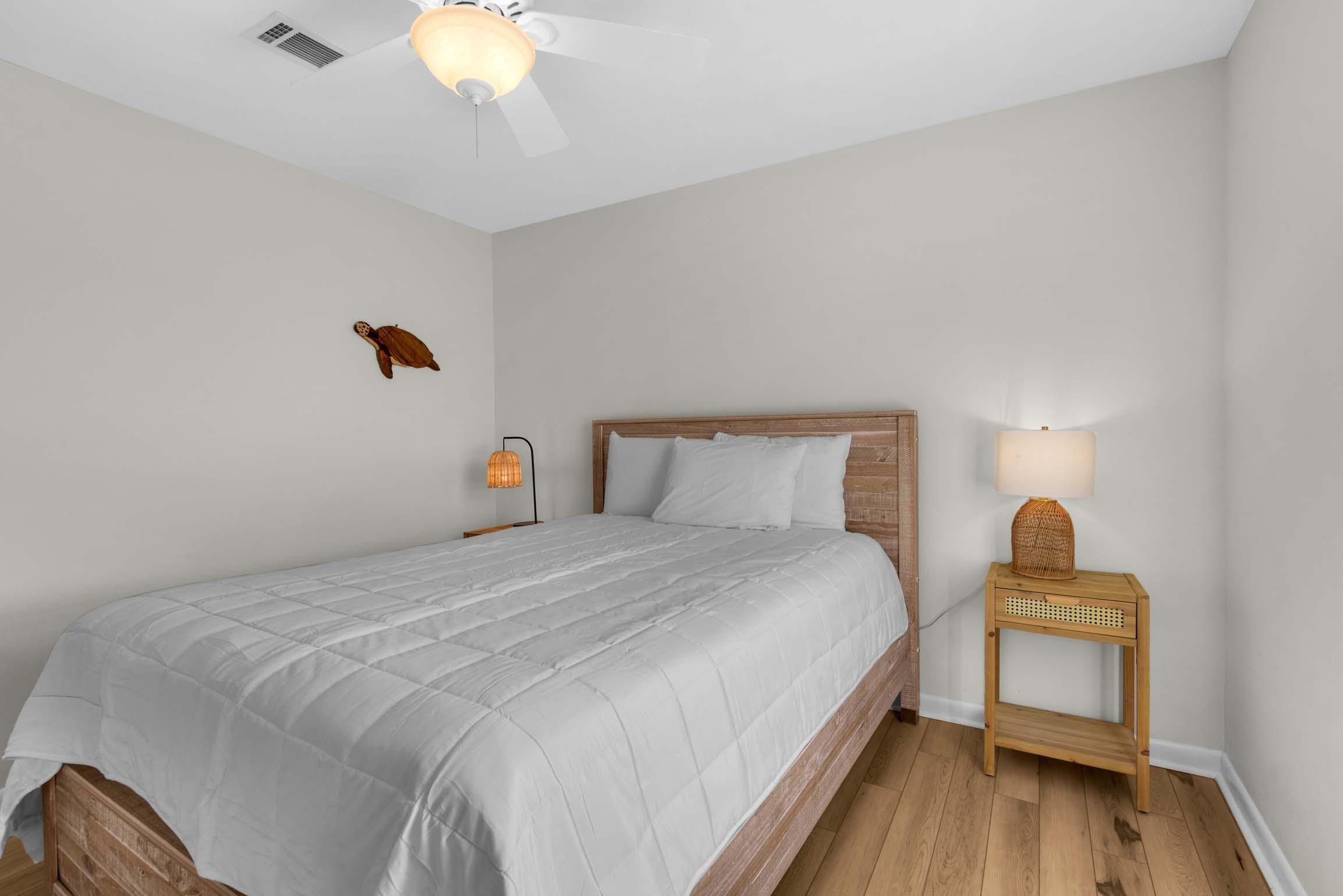 Un dormitorio con cama, mesita de noche, lámpara, ventilador de techo y un adorno en la pared.