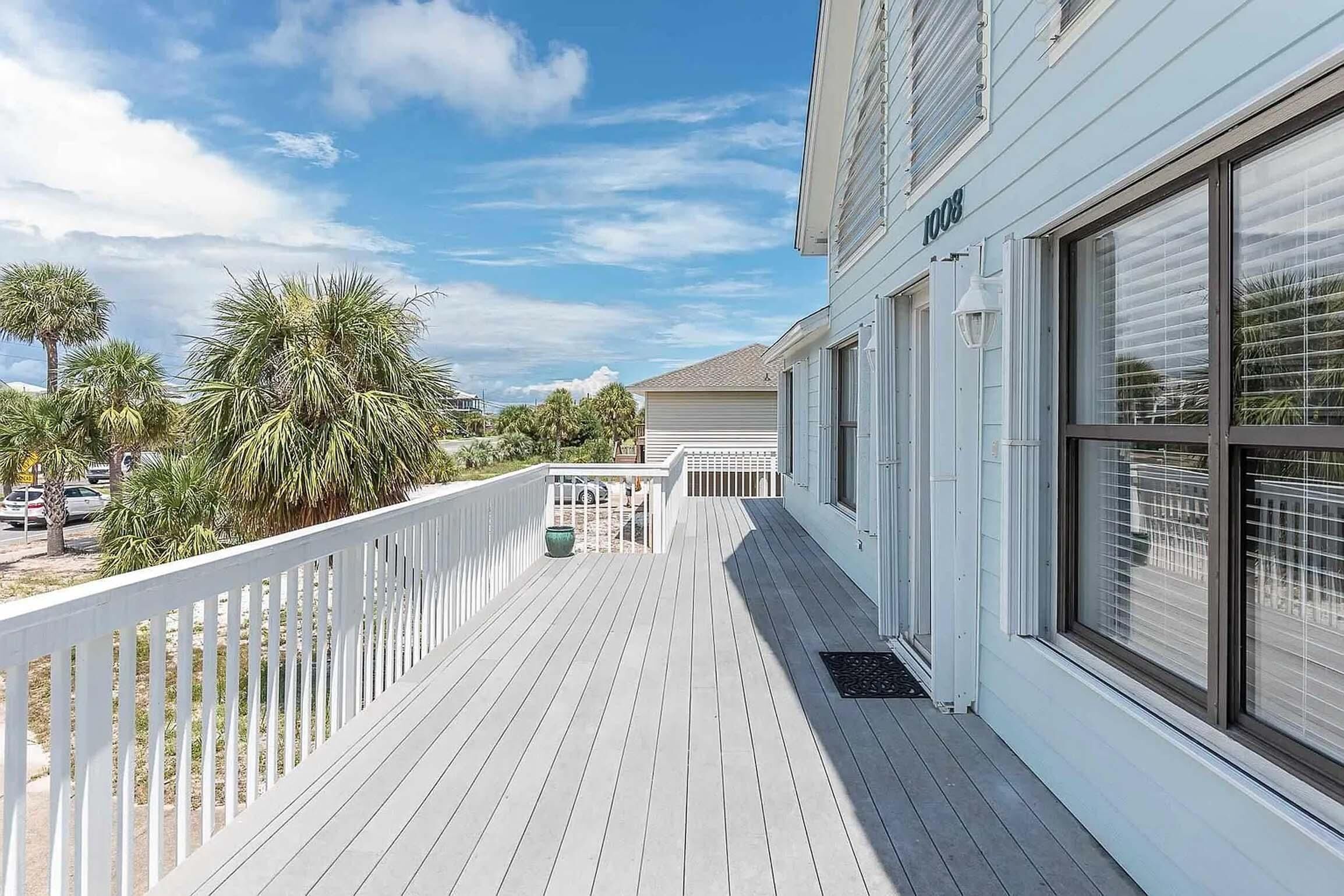 A wooden deck with a white railing, a mailbox, and a street view with palm trees and parked cars.