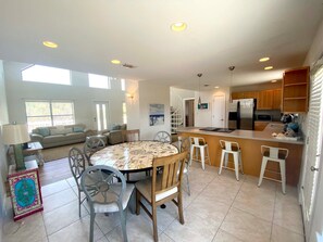 A spacious living area with a round dining table, a sofa, and a kitchen area with a refrigerator and bar stools. - Blue Heron (Pensacola Beach)