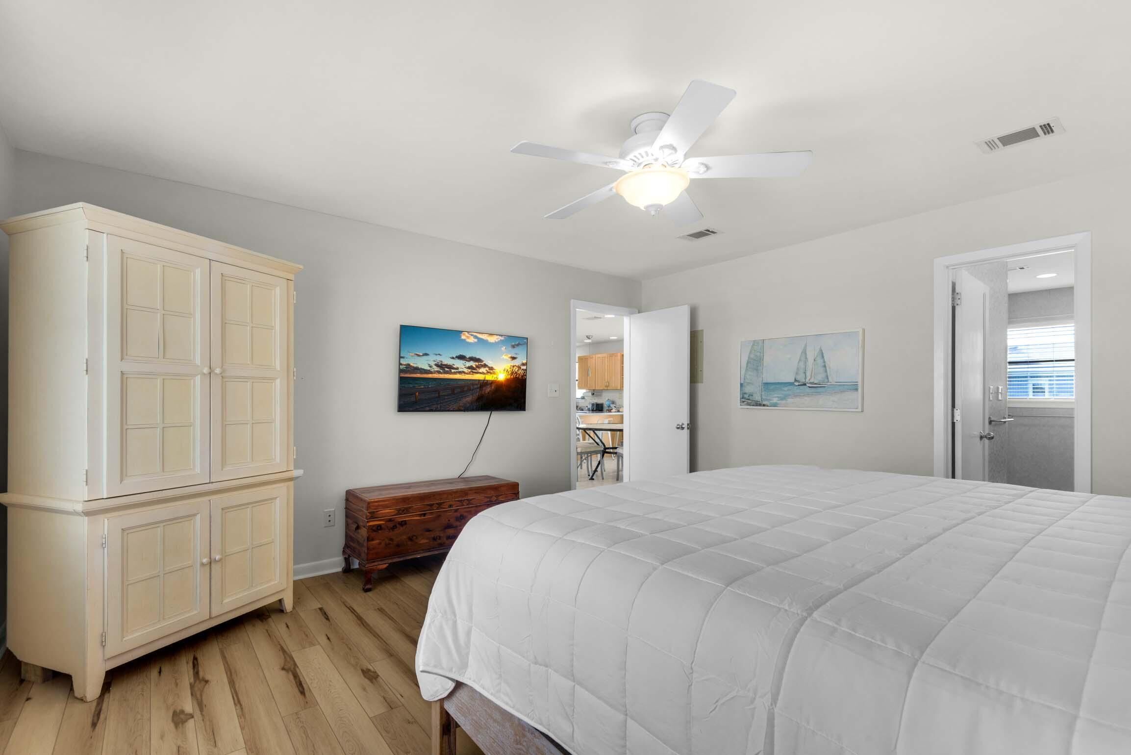 Une chambre à coucher avec un lit, un ventilateur de plafond, une armoire et des œuvres d’art accrochées aux murs.