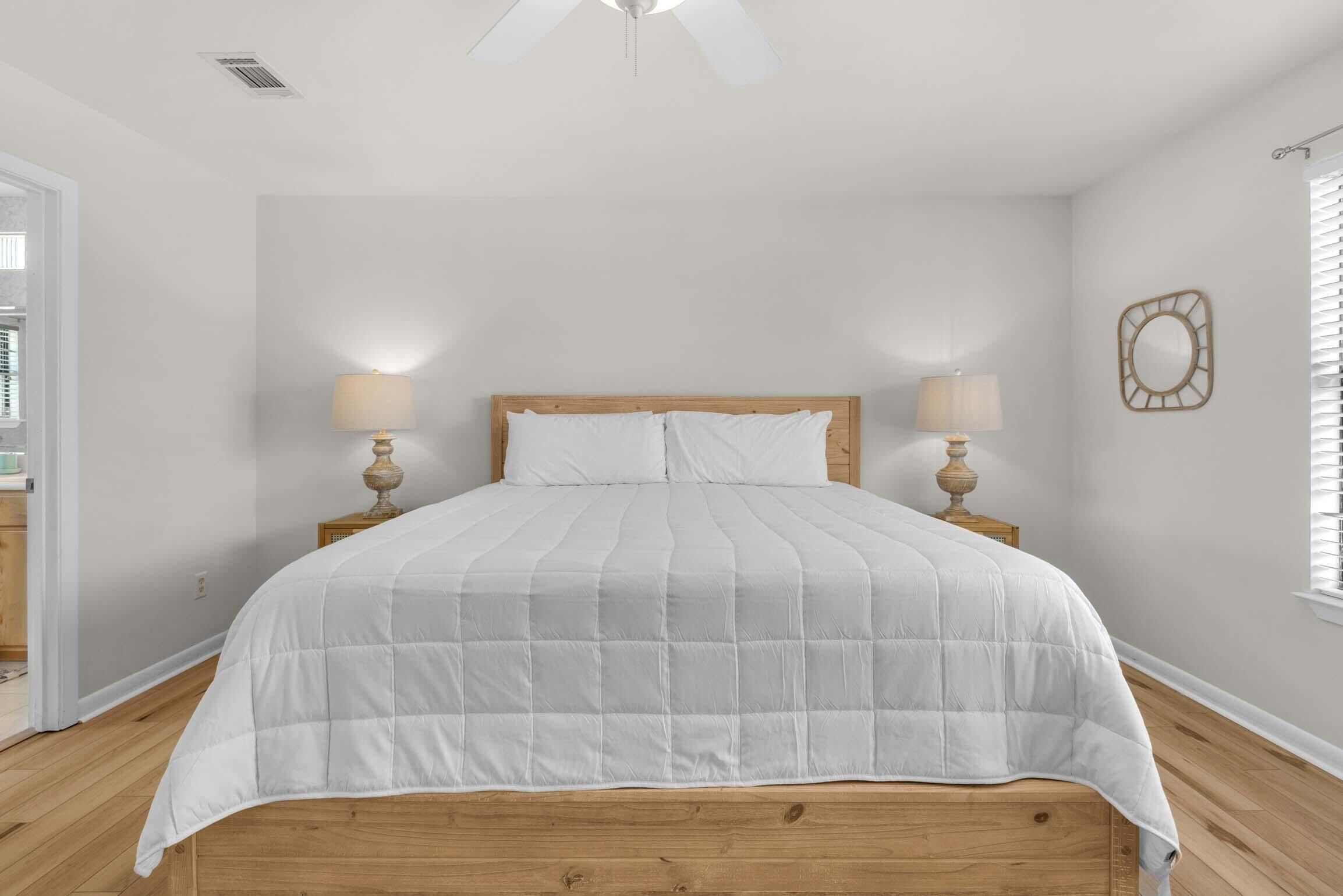 A bedroom with a wooden bed, two bedside lamps, a ceiling fan, and a window with blinds.