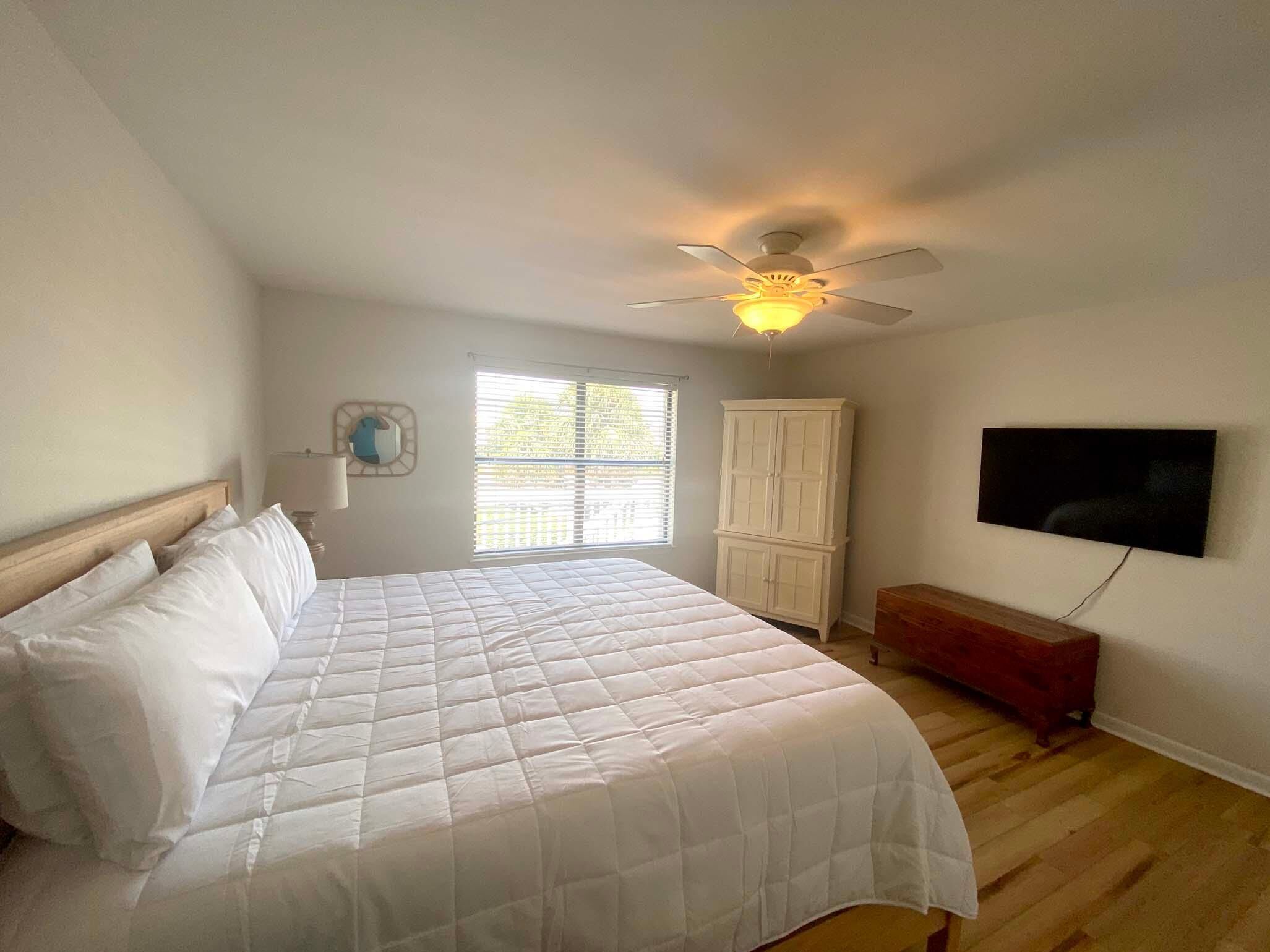 A bedroom with a bed, a ceiling fan, a window, a TV, and a cabinet.