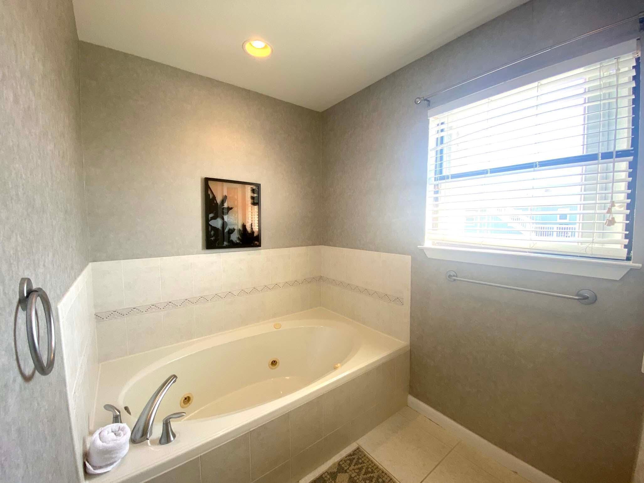 A modern bathroom with a freestanding bathtub, a towel rack, a picture on the wall, and a window with blinds.