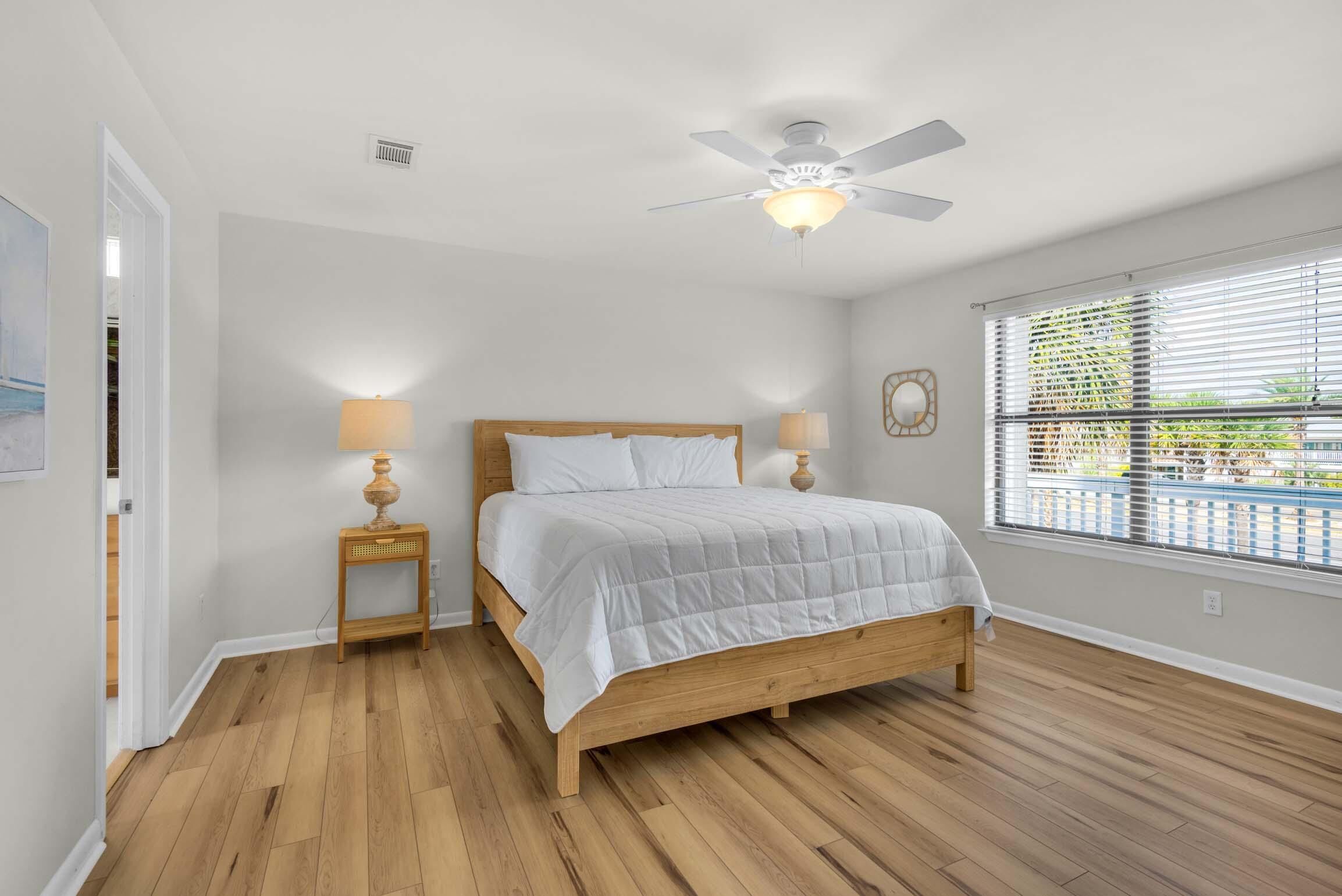 Un dormitorio con una cama de madera, dos lámparas de noche, un ventilador de techo y una ventana con persianas.