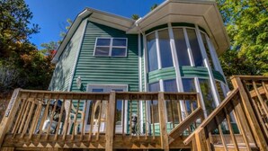 A green house with a curved corner, a wooden deck, and a clear blue sky. - 21A Edelweiss w/ Hot Tub (Gatlinburg)