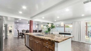 A modern kitchen with a granite countertop, wooden cabinets, and a central island. - 5BR w/Heated Pool & Spa Next To Downtown Chandler (Chandler)