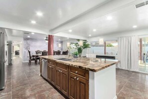 A modern kitchen with a granite countertop, wooden cabinets, and a central island. - 5BR w/ Heated Pool & Spa Next To Downtown Chandler (Chandler)