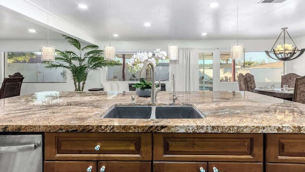 A kitchen with granite countertops, wooden cabinets, and a large island with a sink. - 5BR w/Heated Pool & Spa Next To Downtown Chandler (Chandler)