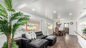 A modern living room with a black leather sofa, a dining table with chairs, and a large potted plant. - 5BR w/Heated Pool & Spa Next To Downtown Chandler (Chandler)