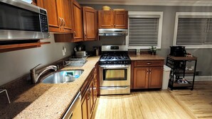A kitchen with wooden cabinets, stainless steel appliances, a granite countertop, and a window with blinds.