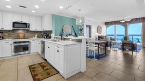 A modern kitchen with white cabinets, a large island, and a dining area with a view. - Portofino Island Resort 3-706 (Pensacola Beach)