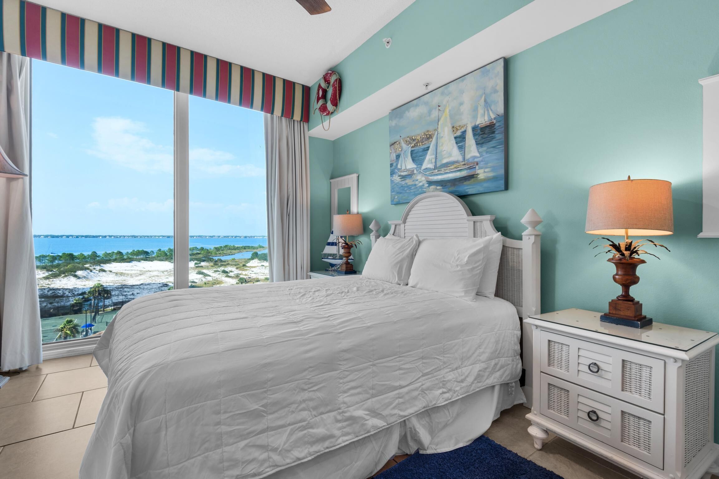A bedroom with a large window offering a view of the beach and ocean.