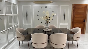 Un comedor moderno con una mesa de vidrio rodeada por seis sillas, un reloj decorativo y una puerta de madera.