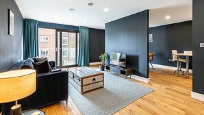 A modern living room with a sofa, a coffee table, a TV, and a dining area with chairs.
