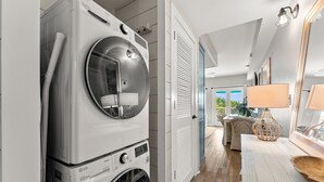 Een wasruimte met gestapelde wasmachines, een houten vloer, een eethoek met een tafel en stoelen, en uitzicht op groen buiten.
