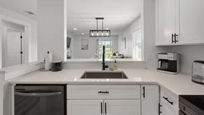 Una cocina moderna con armarios blancos, un lavamanos de acero inoxidable, una cafetera y un lavavajillas.