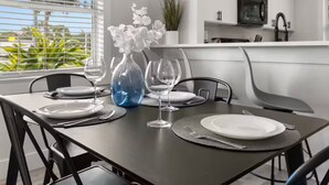 Una mesa de comedor preparada con platos, cubiertos y copas de vino, con un jarrón de flores blancas.