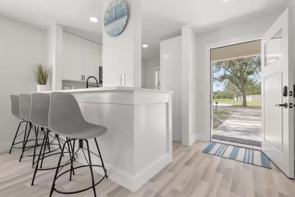 A modern kitchen with a central island, bar stools, and a clock on the wall.