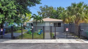 A gated residential area with a house, a fenced yard, and a palm tree. - Stylish 2BR Retreat in Miami's Design District! (Miami)