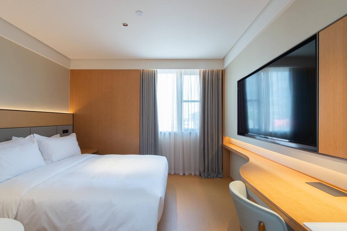 Een hotelkamer met een groot bed, een flatscreen-tv, een bureau en een raam met gordijnen.
