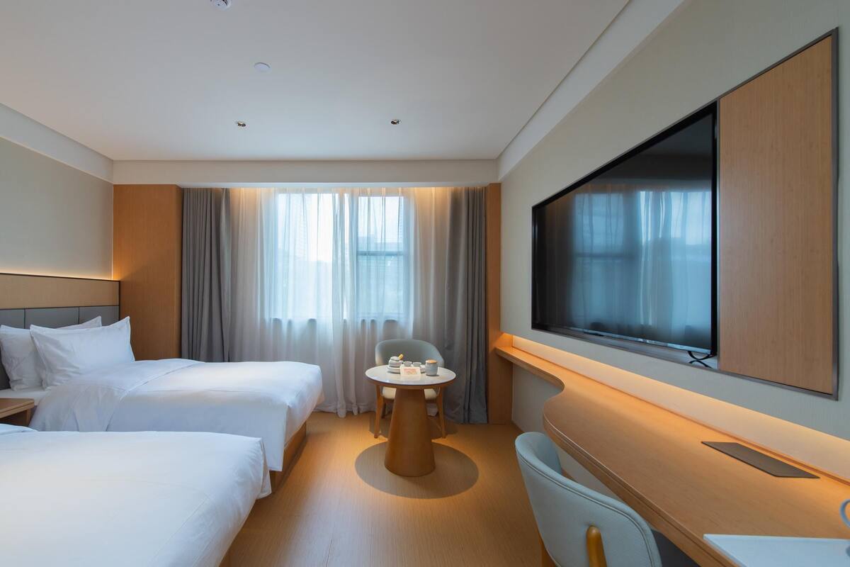 Een hotelkamer met twee bedden, een televisie, een klein tafeltje met spullen, en een groot raam met gordijnen.