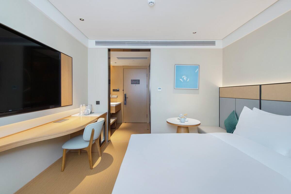 Een moderne hotelkamer met een groot bed, een bureau met stoel, een klein rond tafeltje en een televisie.