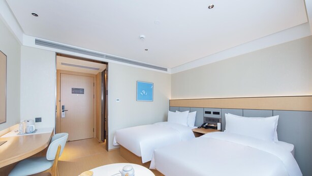 Ein Hotelzimmer mit zwei Betten, einem Schreibtisch, einem Stuhl und einem kleinen Tisch mit Tee-Zubehör.