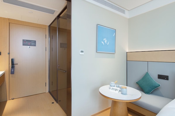 A hotel room with a wooden door, a glass partition, a round table with a blue cushion, and a framed picture on the wall. - Ji Guangzhou Beijing Road Pedestrian St Cangbian (Guangzhou)