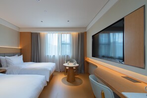 Une chambre d’hôtel avec deux lits, une télévision, une petite table avec quelques objets et une grande fenêtre avec des rideaux.