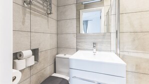 A modern bathroom with a white sink, toilet, and shower. There are toilet paper rolls and a towel rack visible. - Stylish & Petit Studio flat w/great tube connectio (Greater London)