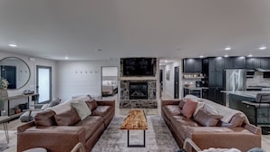 A modern living room with two leather sofas, a wooden coffee table, and a stone fireplace. - Cozy Haven - 4 En-Suite BR + Hot Tub + Fire Pit (Lead)