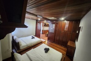 Una habitación con dos camas, piso de madera y una kitchenette al fondo.