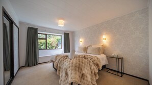 Een slaapkamer met een groot bed, twee bedlampen, een raam met gordijnen en een vloerbedekking.