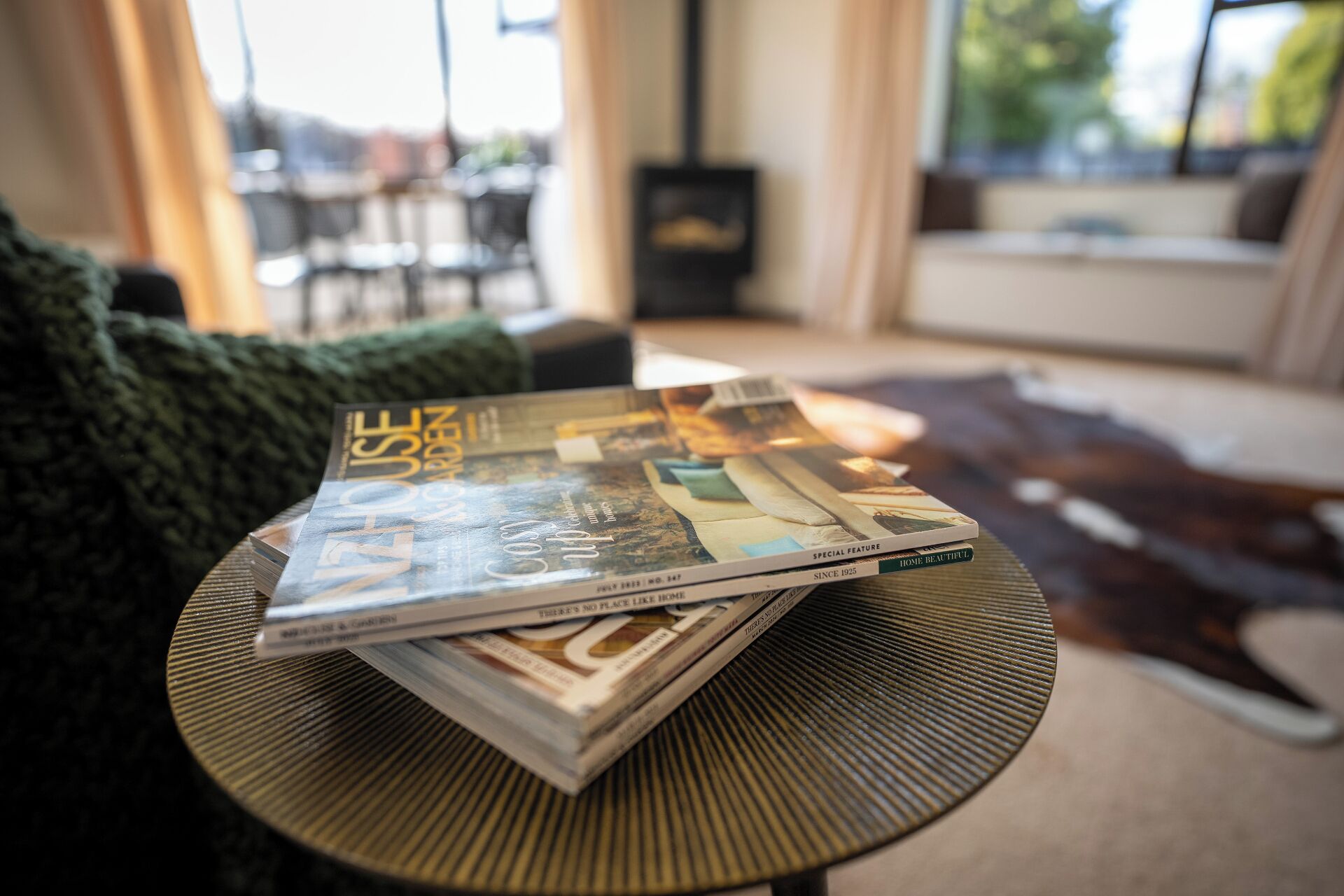 Un magazine est posé sur une table ronde dans une pièce qui contient un canapé et offre une vue sur l’extérieur.