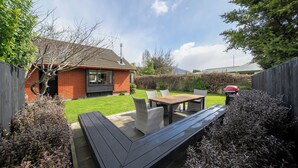 Een achtertuin met een houten bankje, een kleine tafel en een barbecue.