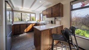 Een moderne keuken met houten kasten, een groot eiland en uitzicht op een tuin door de ramen.