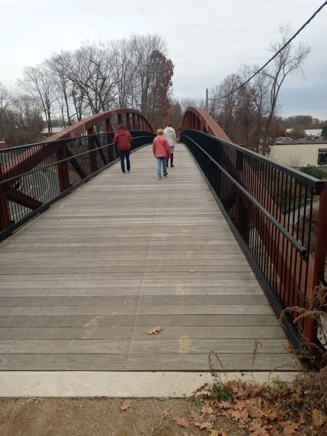A wooden pedestrian bridge with metal railings, surrounded by trees and buildings.