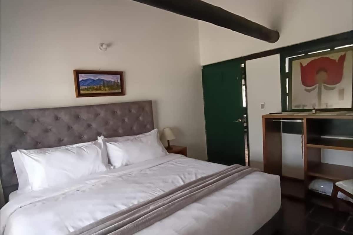 A bedroom with a large bed, a headboard, a nightstand, a dresser, a mirror, and a painting on the wall.