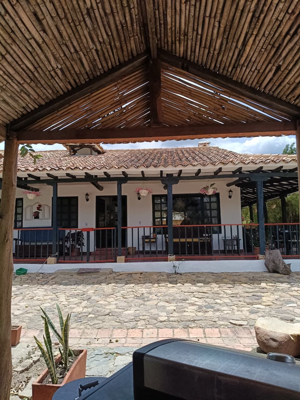 A covered outdoor area with a tiled roof, stone flooring, and a building with a white facade and dark trim.