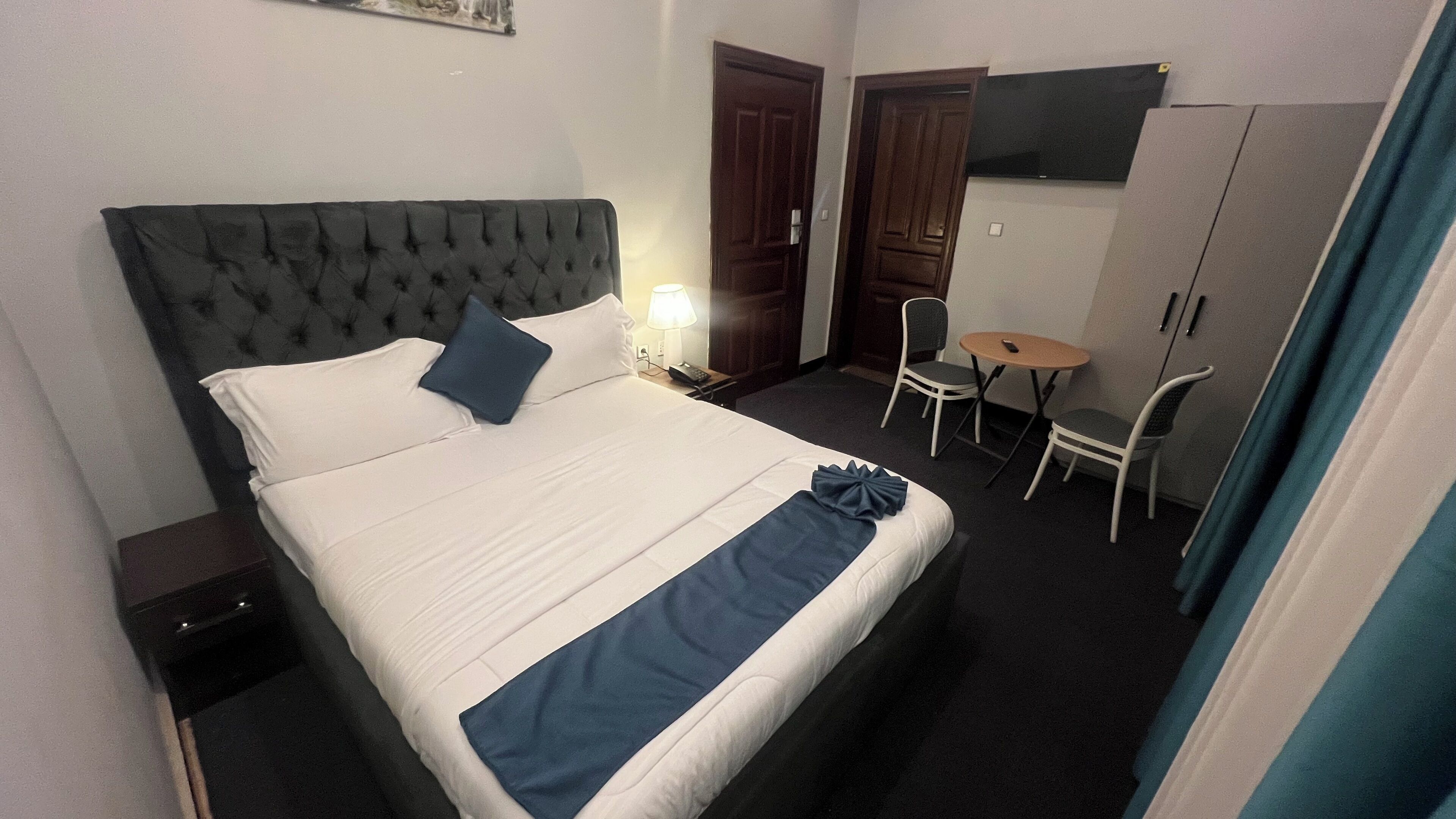 Una habitación de hotel con cama, escritorio, silla, armario y televisor en la pared.