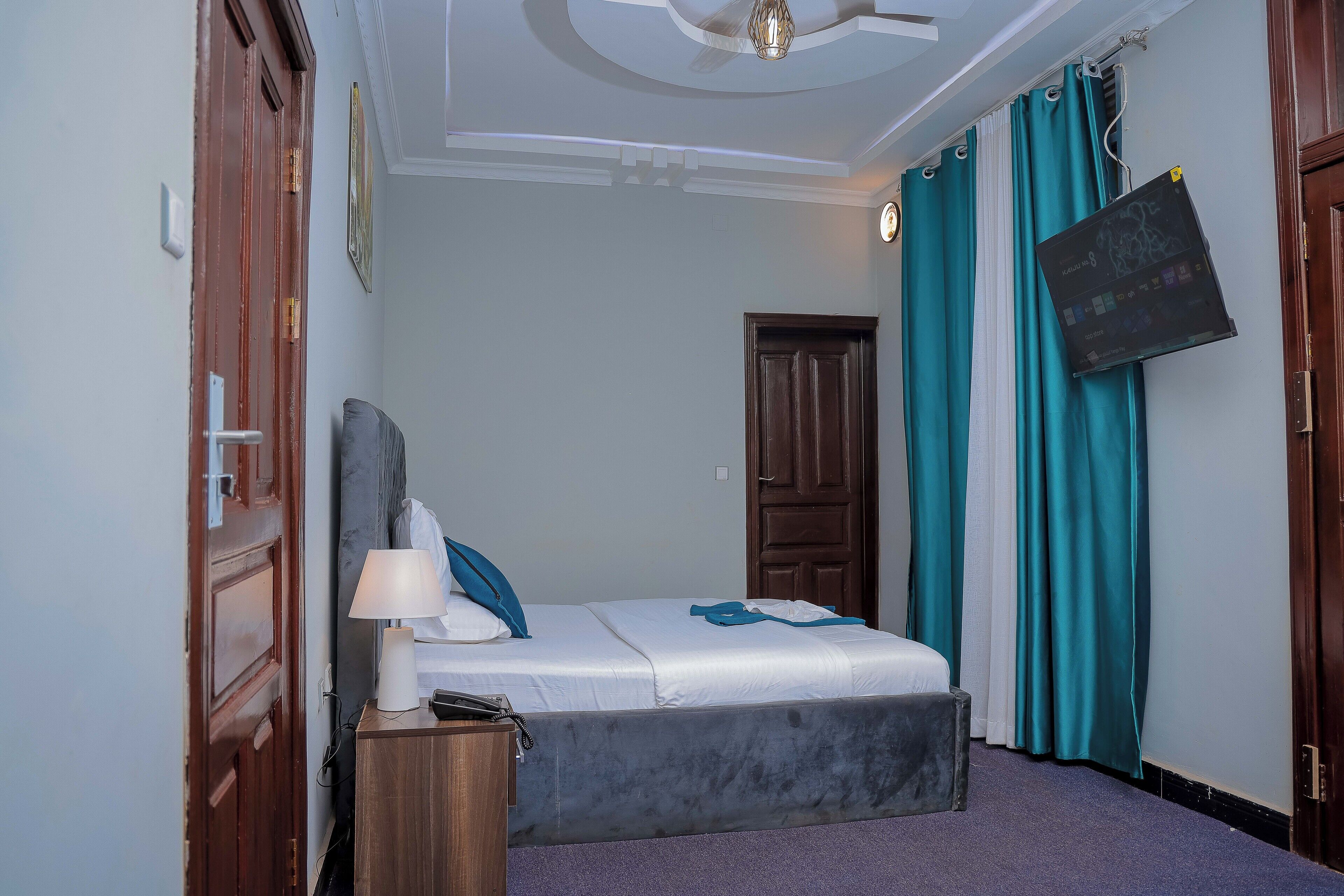A bedroom with a bed, a bedside table, a lamp, a ceiling fan, and teal curtains.