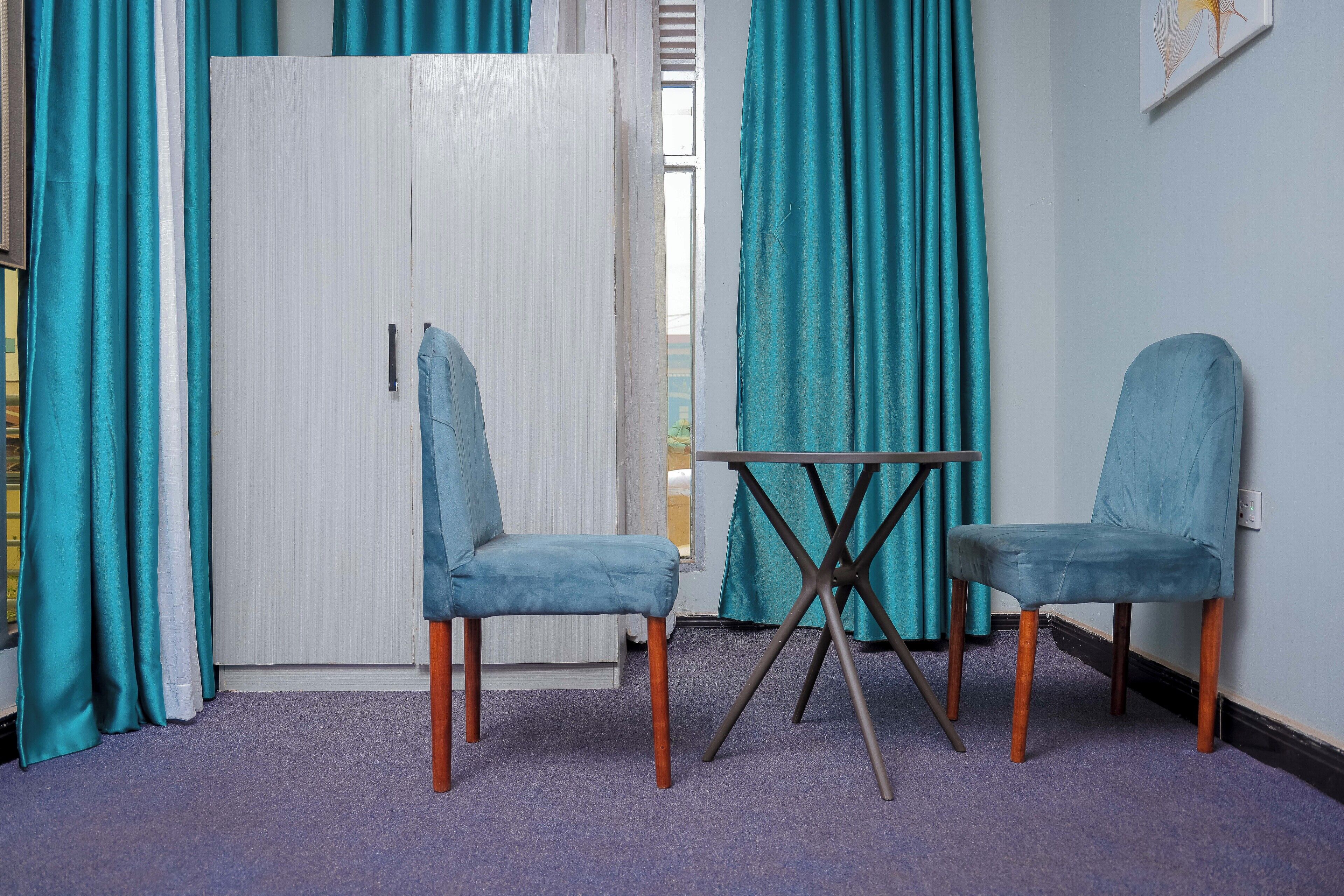 Une pièce avec des rideaux de couleur turquoise, une porte blanche, deux chaises bleues et une petite table.
