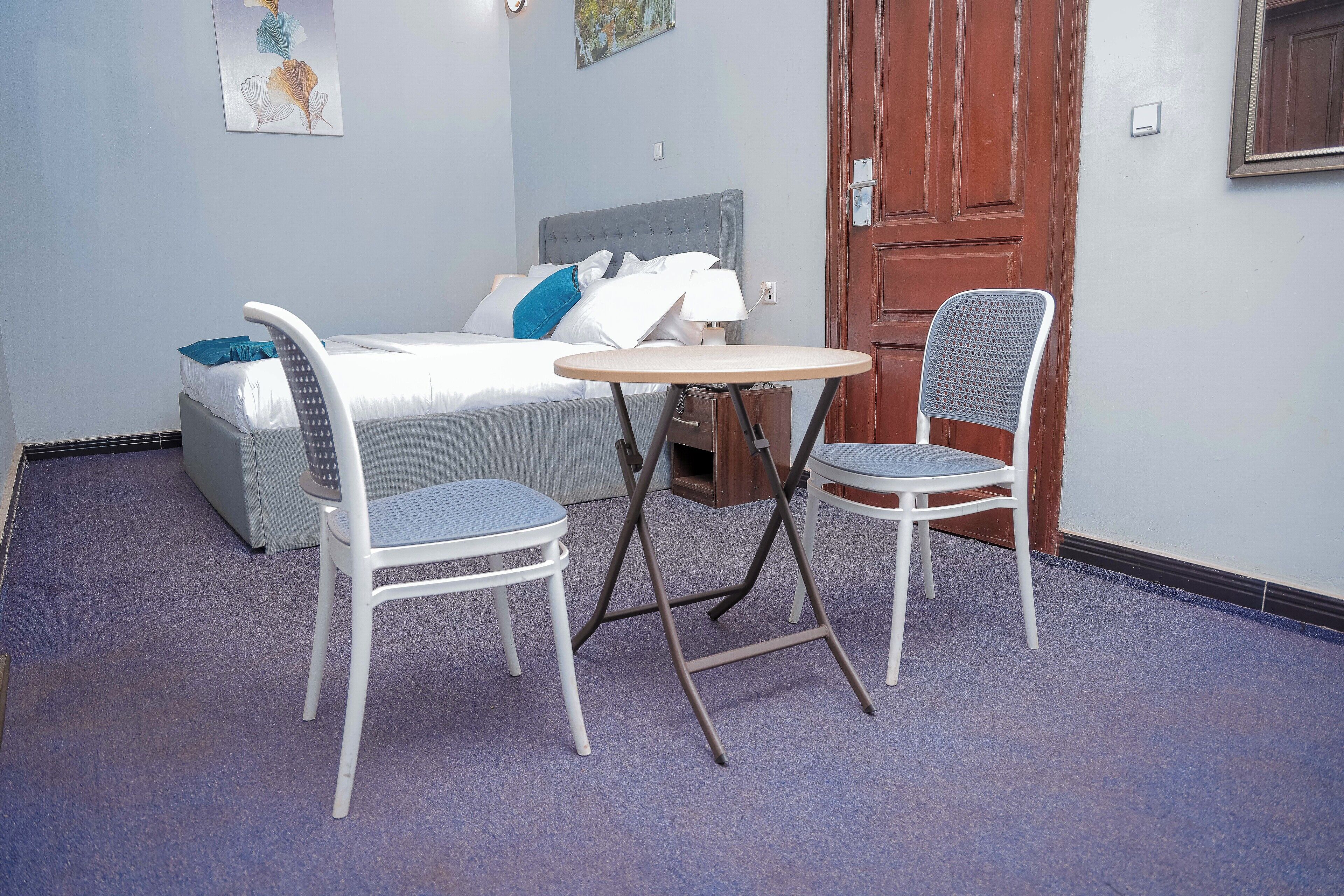 A bedroom with a bed, two chairs, a small table, and a wooden door.
