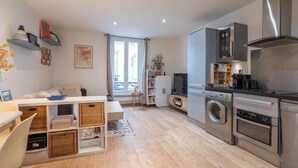 A modern kitchen with stainless steel appliances, a dining area with a white table and wicker baskets, and a cozy living space with a sofa and decorative items. - Cozy Hideaway in a Quiet Paris Passage (Paris)
