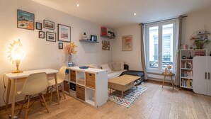 A cozy living room with a white sofa, a small wooden table, a desk with a lamp, and a bookshelf. - Cozy Hideaway in a Quiet Paris Passage (Paris)